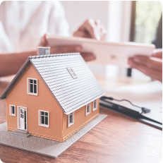 A model of a house with people planning things in the background